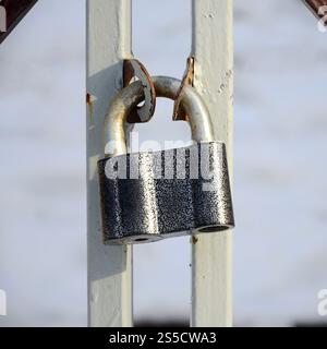 A large gray padlock hangs on a metal gate Stock Photo