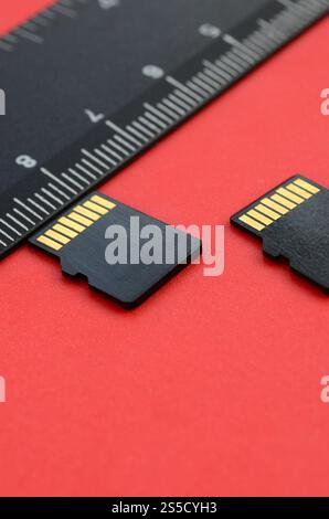 Two small micro SD memory cards lie on a red background next to a black ruler. A small and compact data and information store Stock Photo