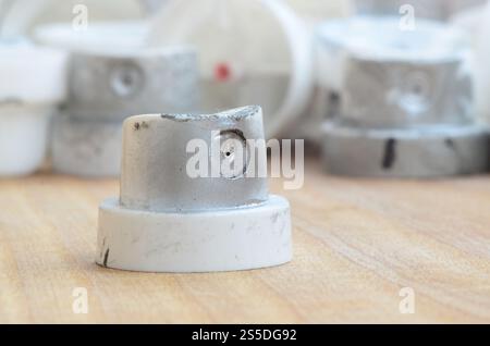 Several plastic nozzles from a paint sprayer that lie on a wooden surface against a gray wall background. The caps are smeared in chrome paint. The Stock Photo