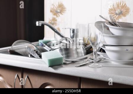 A huge pile of unwashed dishes in the kitchen sink and on the countertop. A lot of utensils and kitchen appliances before washing. The concept of Stock Photo