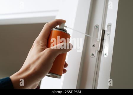 closeup of a man spraying some lubricating oil on the hinge of a white indoors door Stock Photo