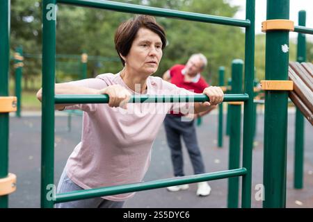Mature woman doing push-ups from the crossbar on outdoor sports ground Stock Photo