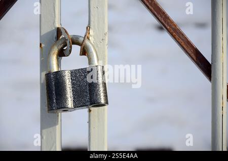 A large gray padlock hangs on a metal gate Stock Photo