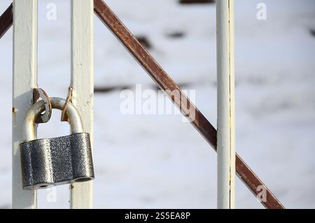 A large gray padlock hangs on a metal gate Stock Photo