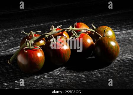 kumato cherry tomato branch on black wood background Stock Photo