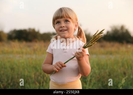 Cute little girl with plants at meadow. Child enjoying beautiful nature Stock Photo