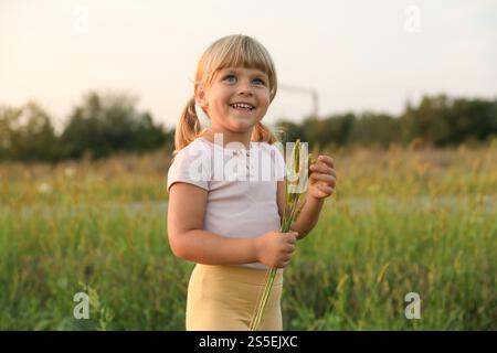 Cute little girl with plants at meadow. Child enjoying beautiful nature Stock Photo