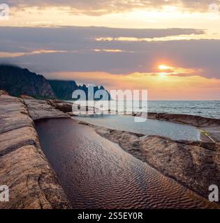 Stony beach with tidal baths at Ersfjord, Senja, Norway. Summer polar day night coast. The dragon teeth rock in far. Stock Photo