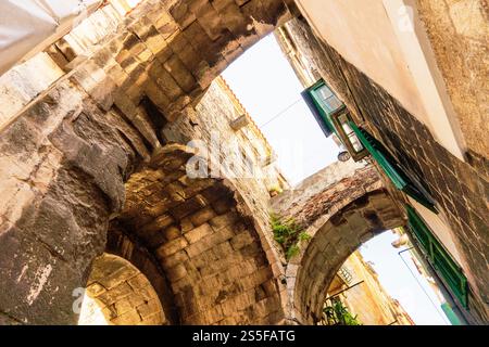 Sunlit stone alley with arches and green windows in an old city of Split, Croatia Stock Photo