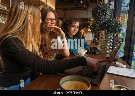 Three women engaging in conversation at a cafe table while one operates a laptop, Berlin, Germany Stock Photo