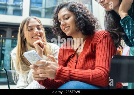 Three smiling women sharing a moment while looking at a smartphone together, Berlin, Germany Stock Photo
