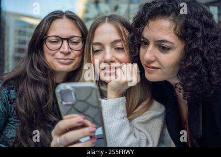 Three women smiling and looking at a smartphone together, Berlin, Germany Stock Photo