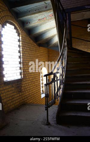 Spiral staircase winding up inside an empty vintage building with brick walls and a large arched window filtering in daylight, Berlin, Germany Stock Photo