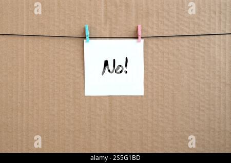 No! Note is written on a white sticker that hangs with a clothespin on a rope on a background of brown cardboard Stock Photo
