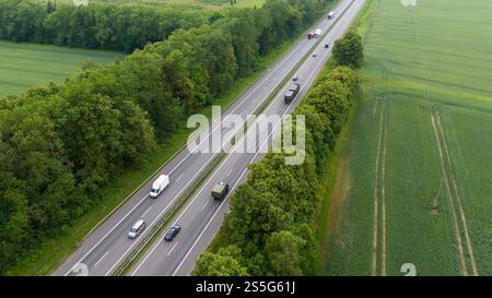Aerial view of a highway running through lush green fields and forests, with several vehicles traveling in both directions. The scene captures the con Stock Photo