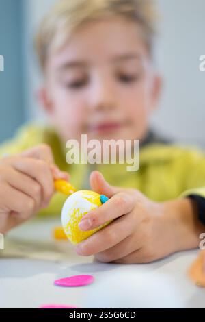 Caucasian child painting and decorating eggs for easter celebration using yellow marker and colorful stickers Stock Photo