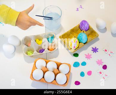 Child is shown painting easter eggs with colorful paints and decorations, getting ready for easter celebration Stock Photo
