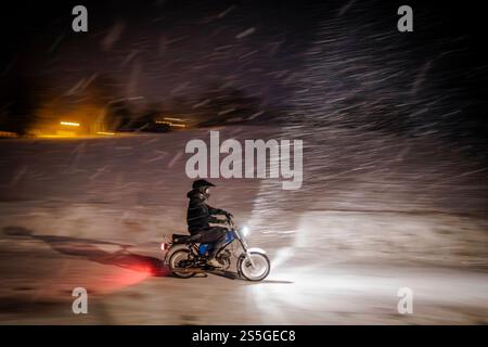 Symbolfoto zum Thema Moped fahren im Winter. Ein Mann faehrt auf einem Simson Moped im starken Schneefall ueber eine verschneite Strasse. Papstdorf, 1 Stock Photo