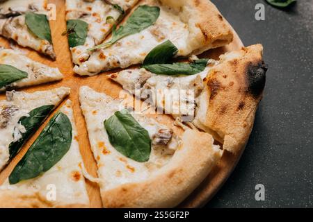 Freshly baked white pizza slices with creamy mushrooms and spinach, served on a wooden plate Stock Photo