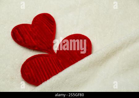 Negative Space Two delicate red hearts made of pipe cleaners with scattered heart glitter on soft fabric background, valentine's day concept backgroun Stock Photo