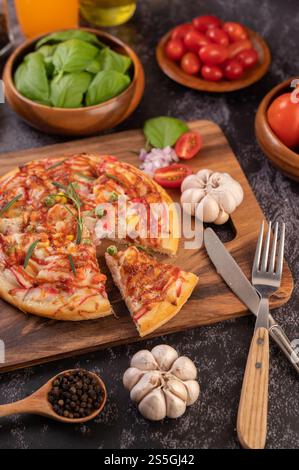 Pizza placed on a wooden plate complete with pepper seeds. Tomatoes and garlic. Selective focus. Stock Photo