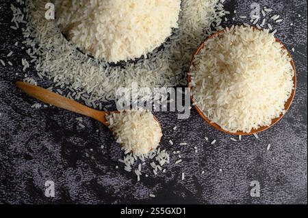 Milled rice in a bowl and a wooden spoon on the black cement floor. Top view Stock Photo