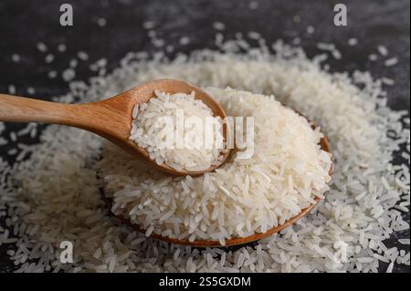 Milled rice in a bowl and a wooden spoon on the black cement floor. Selective focus Stock Photo