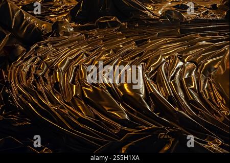 Dark, reflective material with numerous folds and wrinkles, dramatically highlighted by a warm, yellow light source Stock Photo