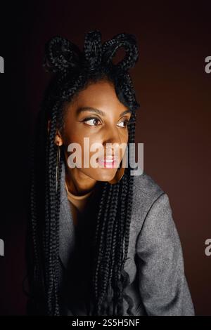 A young woman with intricate braids showcases her beauty through a thoughtful pose in gentle light. Stock Photo
