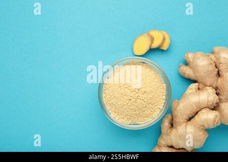 Ginger powder in bowl with fresh ginger root on blue background. Stock Photo