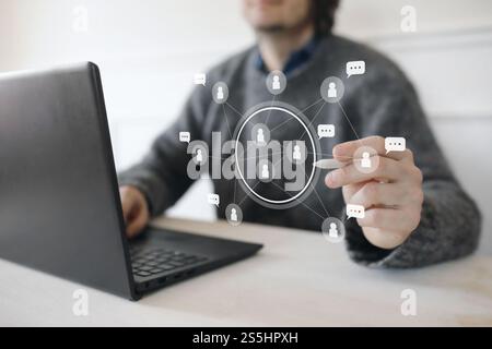 Man in grey sweater with laptop using modern interface with white icons. Social network connection. Chatting, partnership and friendship concept. User Stock Photo