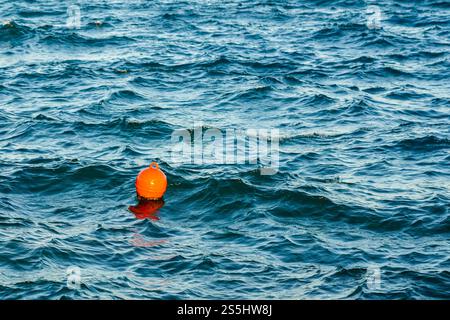 Orange plastic water buoy floating in turquoise sea water, wavy water background Stock Photo
