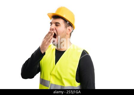 Male constructor wearing fluorescent work vest and safety helmet covering mouth while yawning as tired sleepy concept isolated on white studio backgro Stock Photo