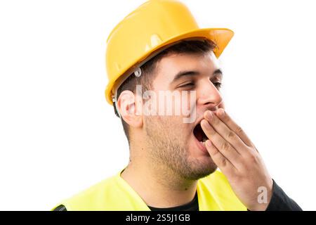 Close-up of sleepy builder man in safety hardhat and fluorescent vest work attire yawning covering mouth with hand isolated on white background Stock Photo