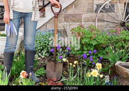 Woman standing in a garden holding garden gloves and spade Stock Photo