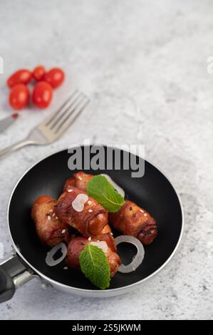 Sausage wrapped in pork belly in a pan with sesame and mint. Selective focus. Stock Photo