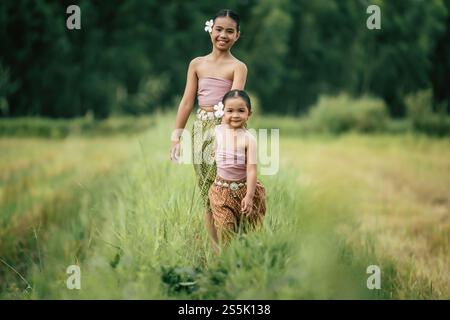 Portrait of two Cute girls in Thai traditional dress walking on rice field, They are smile with happiness and looking at camera, copy space Stock Photo