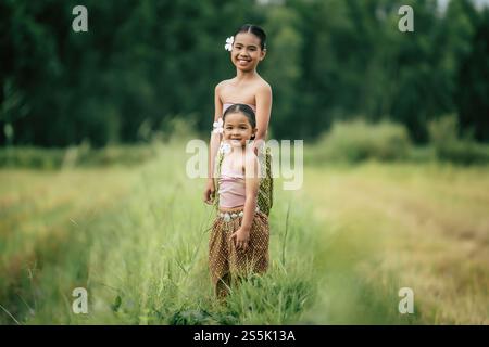 Portrait of two Cute girls in Thai traditional dress walking on rice field, They are smile with happiness and looking at camera, copy space Stock Photo