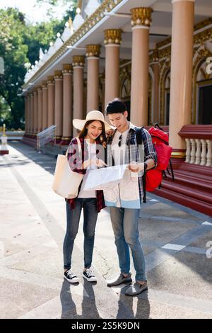 Young Asian backpacker couple in beautiful temple during vacations in Thailand, Pretty woman wearing sombrero point on paper map to checking direction Stock Photo