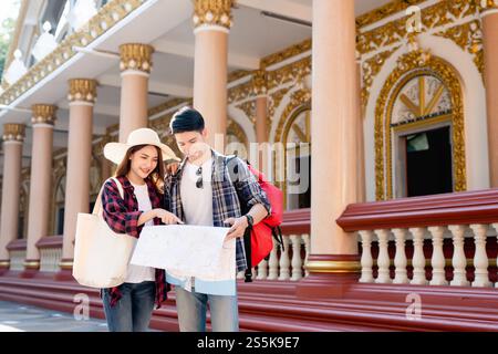 Young Asian backpacker couple in beautiful temple during vacations in Thailand, Pretty woman wearing sombrero point on paper map to checking direction Stock Photo
