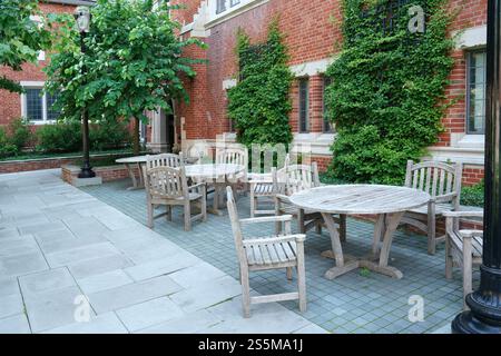 Wooden tables and chairs on a patio beside an ivy covered brick building Stock Photo