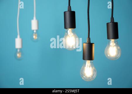 Light bulbs hanging on cords against blue background, selective focus Stock Photo