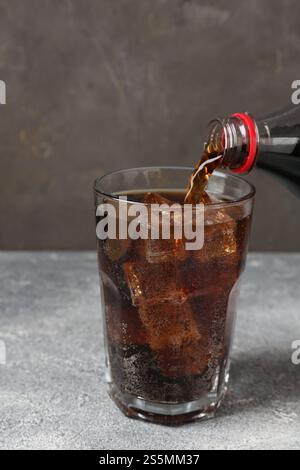 Pouring refreshing cola from bottle into glass on light textured table against grey background, closeup Stock Photo