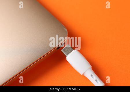 USB charge cable with laptop on orange background, closeup. Space for text Stock Photo
