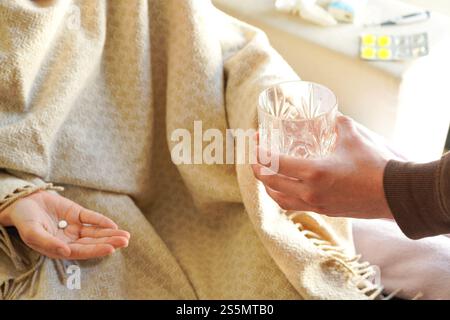 Man handing water to a woman taking cold medicine in bed at home Stock Photo