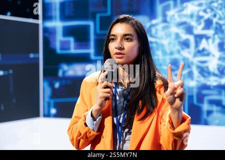 Specialist talking in mic at technology summit, explaining impact of AI technology on world. Speaker presenting ethical practices and understanding of risks and threats associated with AI Stock Photo