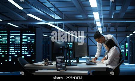 Teamworking colleagues in high tech data center managing and maintaining databases, ensuring data integrity, security and availability. Team of specialists updating server room systems, camera B Stock Photo