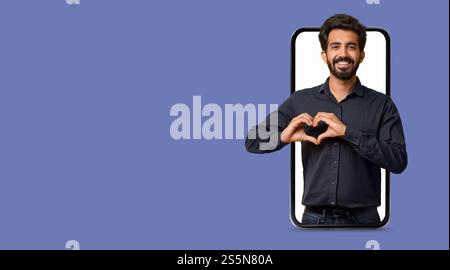 Man making heart gesture with hands inside large smartphone on purple background Stock Photo