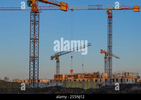 Tower cranes at a construction site with workers and unfinished buildings. Urban development, industrial machinery and construction progress Stock Photo