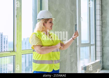 Female industrial worker in protective vest helmet using smartphone at construction site Stock Photo